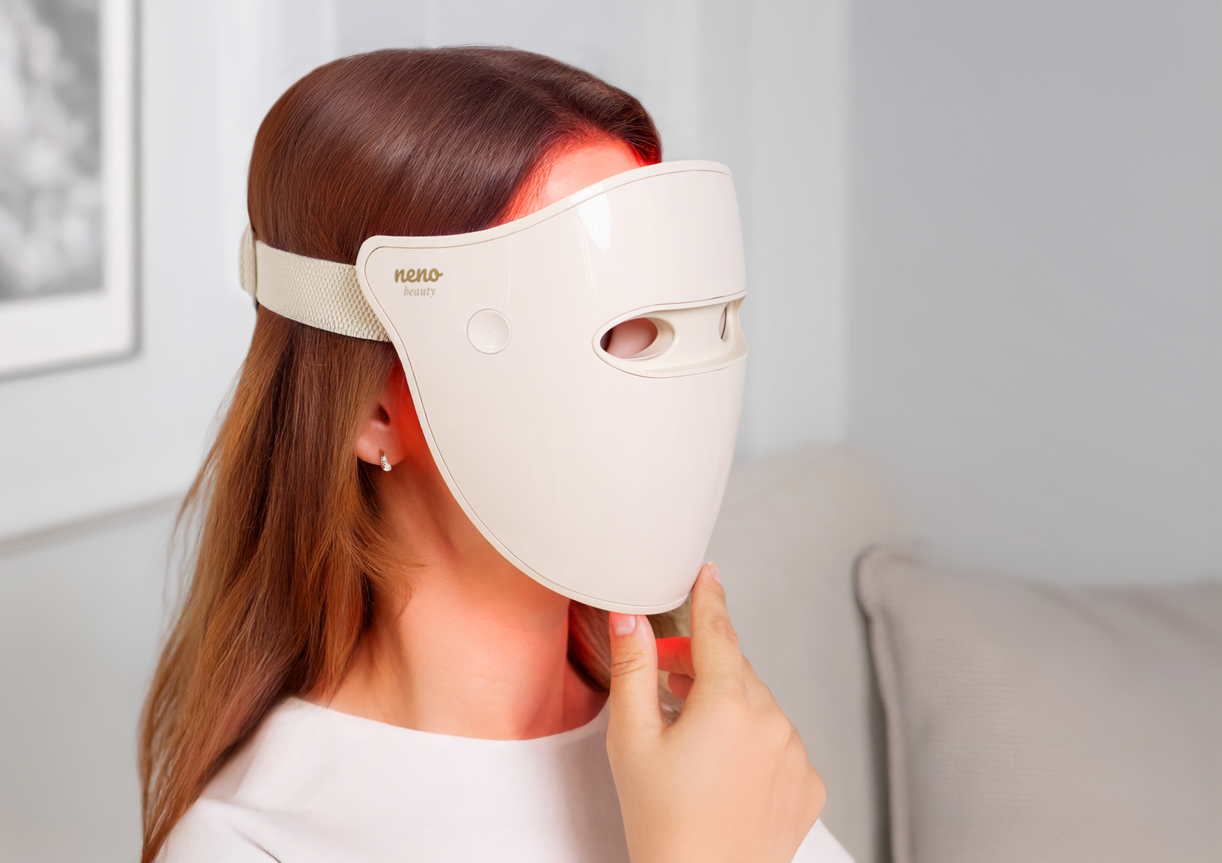 Kobieta siedzi w domu z założoną maską Neno Beauty Alva. Tekst o terapii światłem LED w warunkach domowych, równomiernym działaniu i komforcie stosowania dzięki 220 diodom.