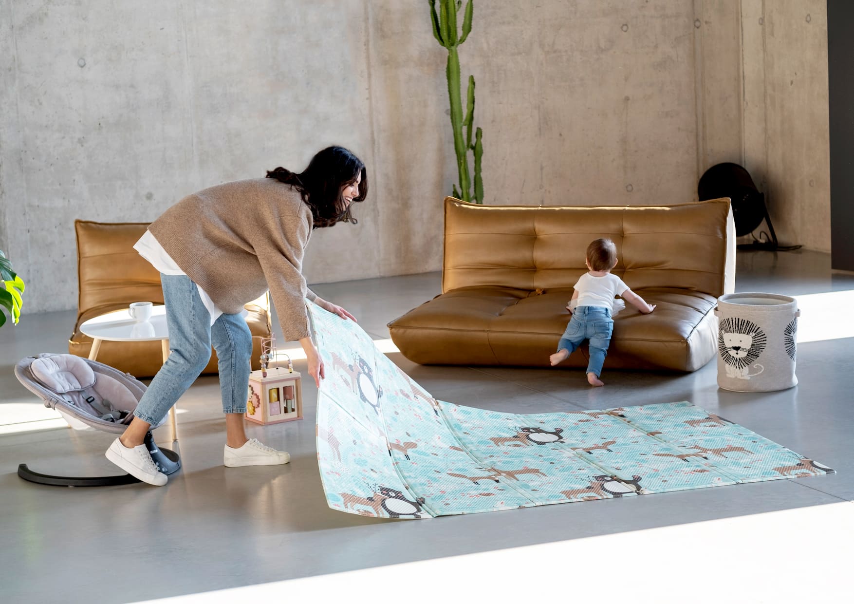 woman unfolding a mat and in the background a child leaning against a couch