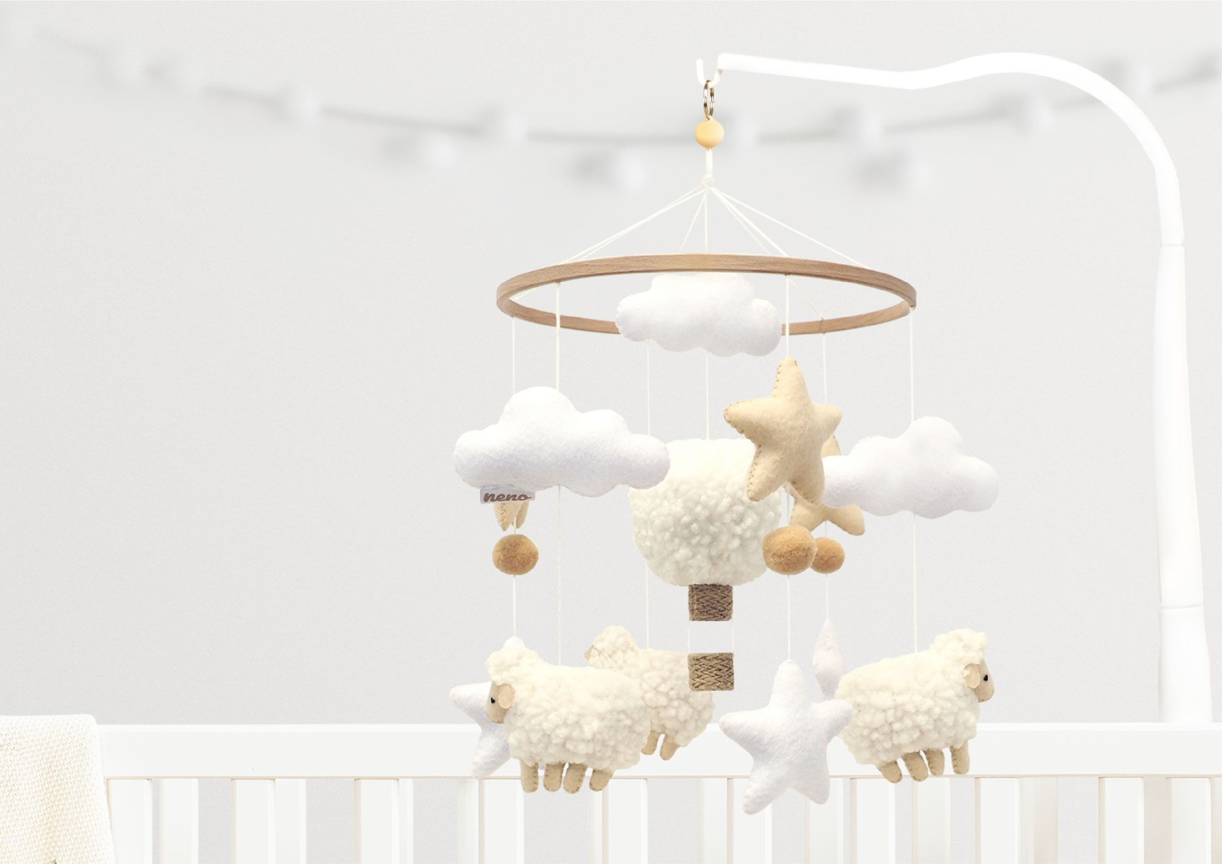 Karuzela Neno Nelu z barankami, chmurkami i gwiazdkami nad łóżeczkiem. Jasne kolory i naturalne materiały tworzą spokojny klimat.