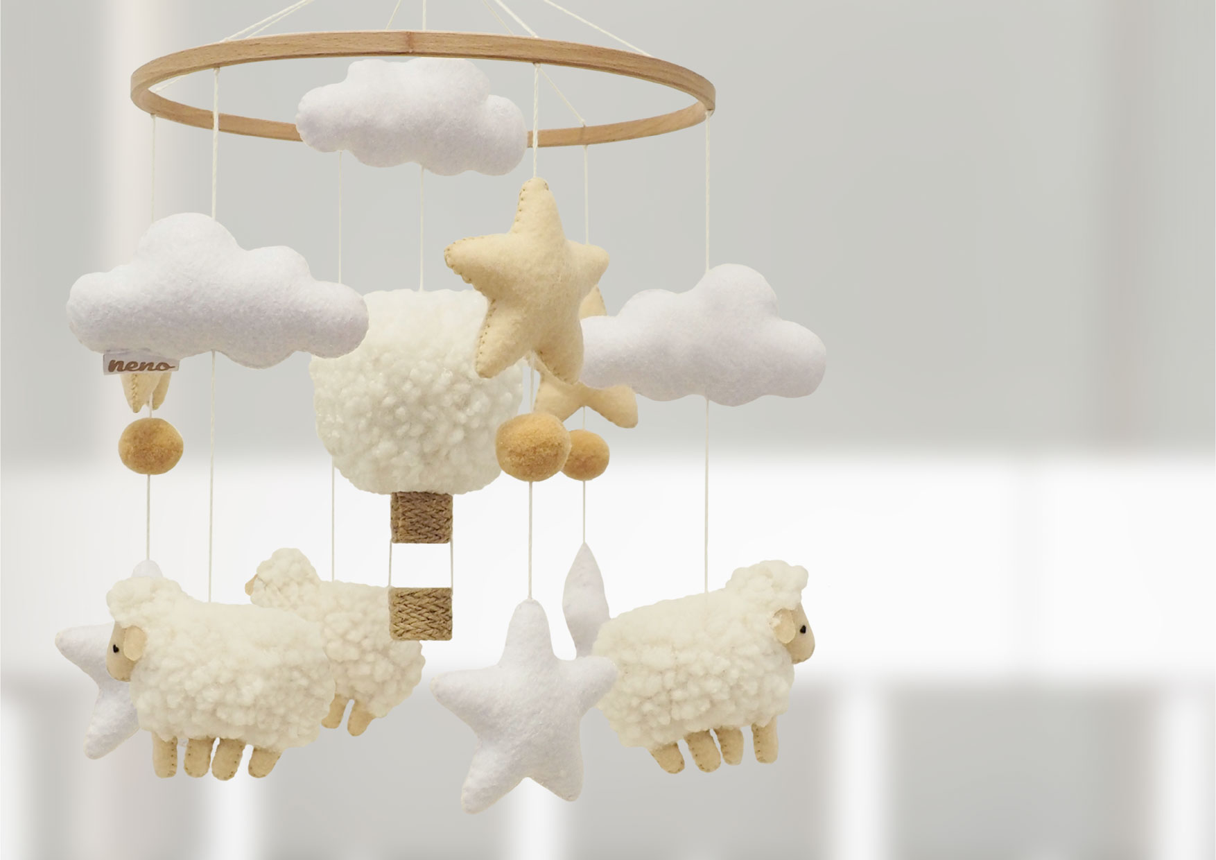 Zbliżenie na filcowe baranki i chmurki karuzeli Neno Nelu. Ręcznie szyte maskotki kołyszą się nad łóżeczkiem, dodając ciepła wnętrzu.
