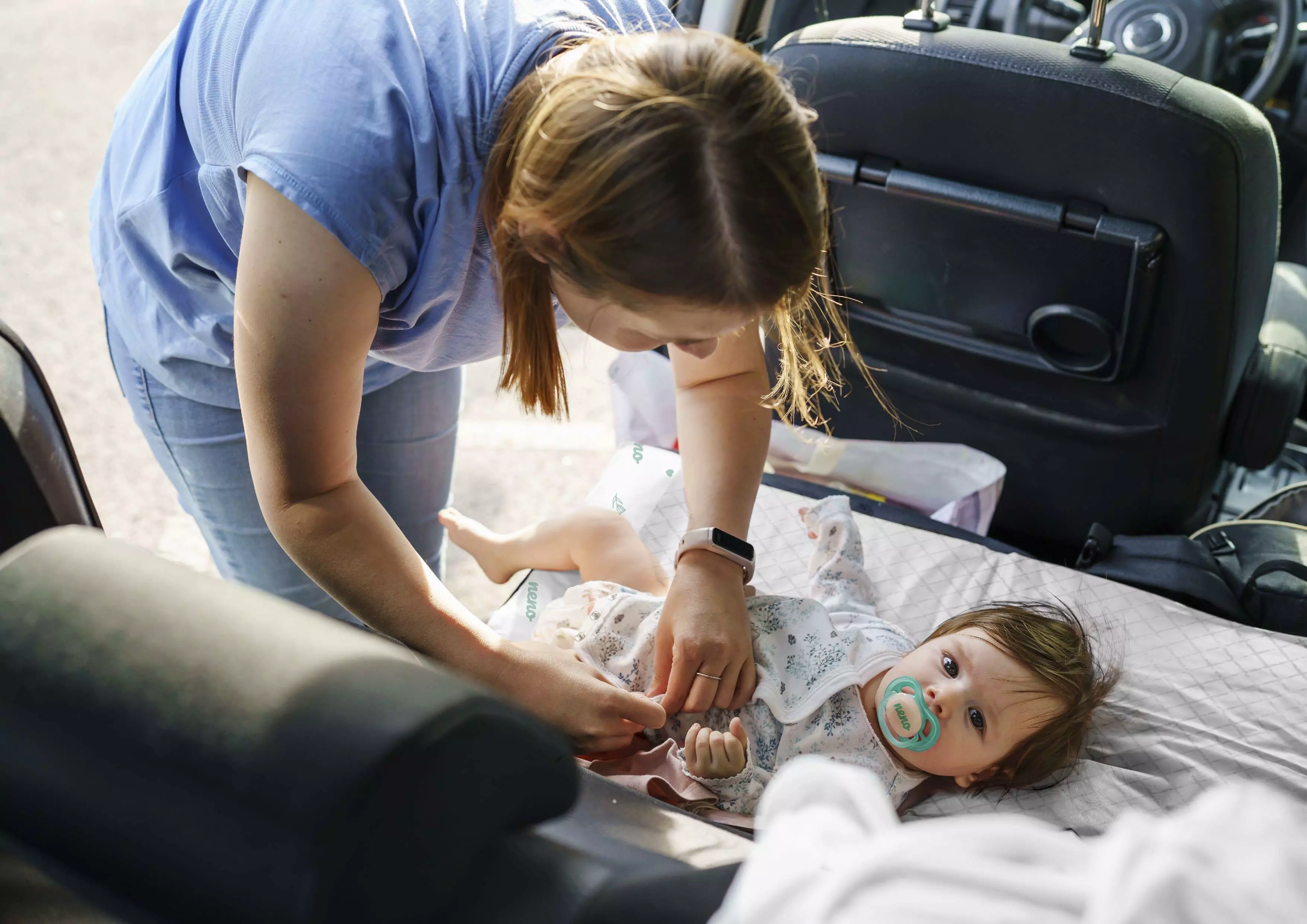 woman changing a toddler in a car with Neno Neo