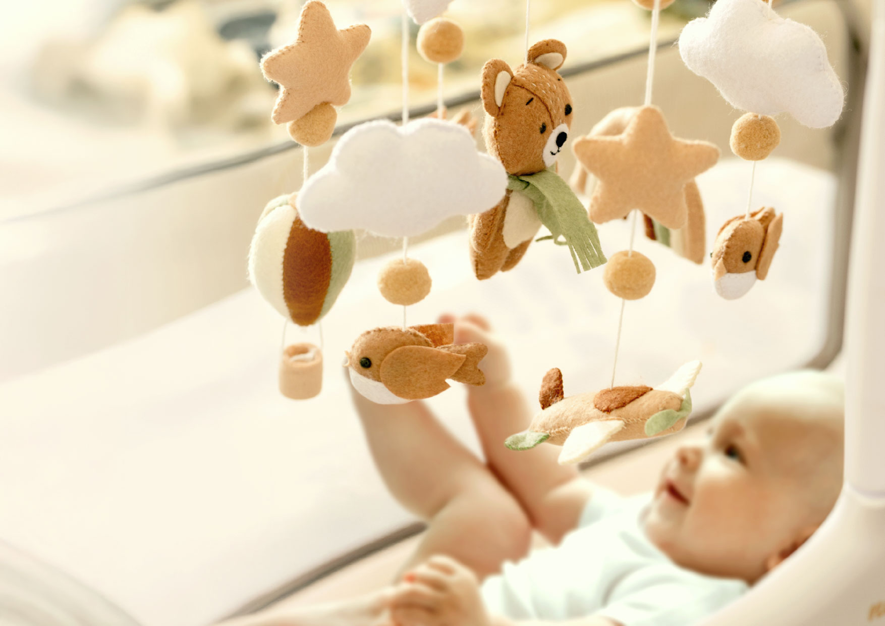Niemowlę obserwuje karuzelę Neno Pico z filcowymi misiami, ptaszkami i gwiazdkami. Przytulna dekoracja pokoju w naturalnych barwach.