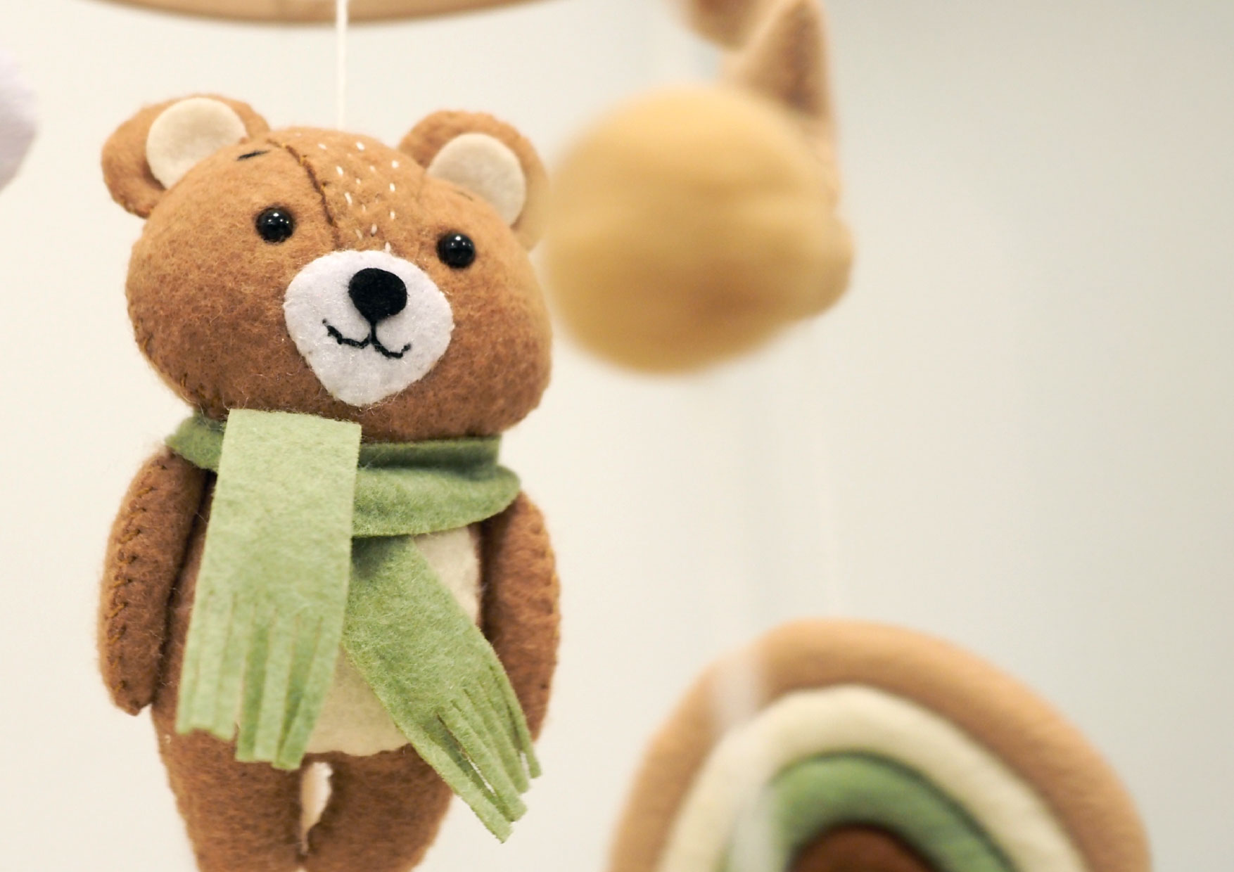 Zbliżenie na filcowego misia z karuzeli Neno Pico. W tle widoczne gwiazdki i tęcza. Ręczne szycie podkreśla staranne wykonanie.