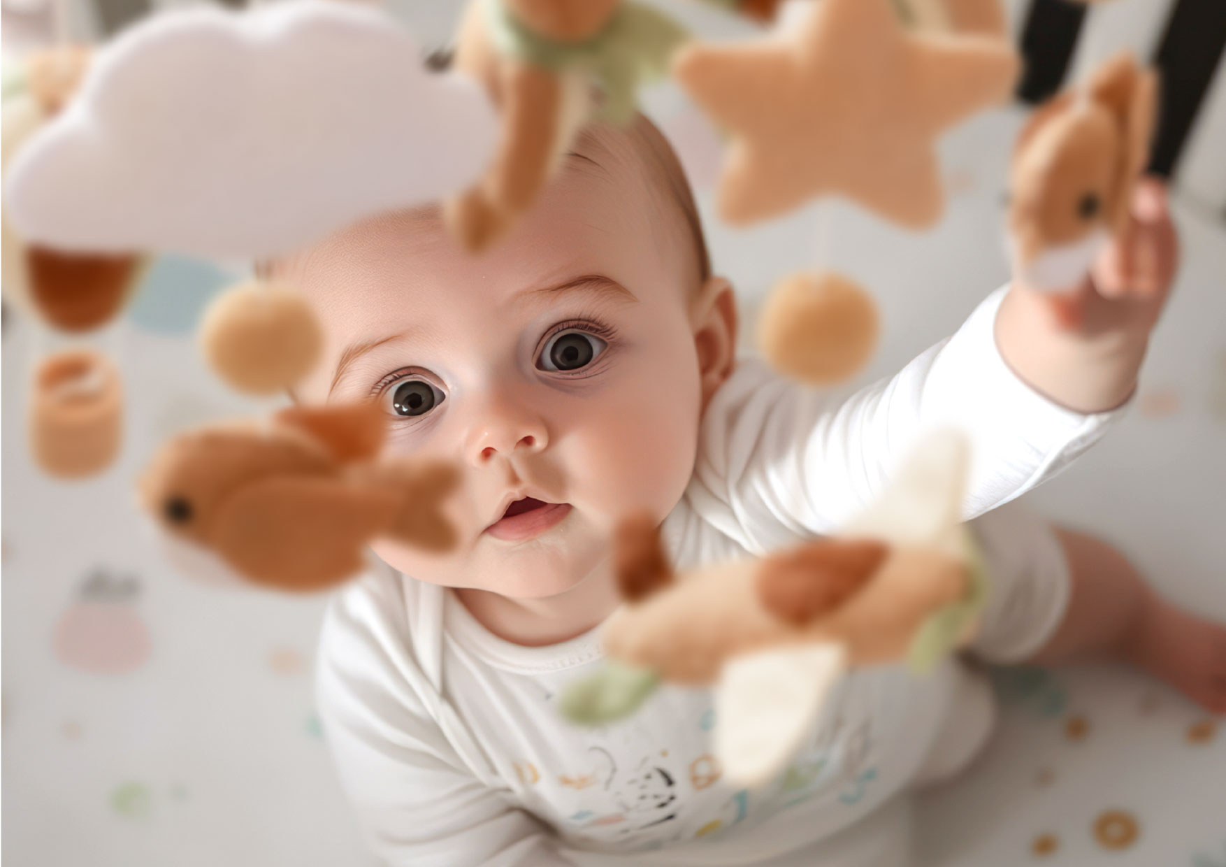 Maluch wyciąga rączki w stronę maskotek karuzeli Neno Pico. Zawieszki wspierają rozwój ruchowy i koordynację.