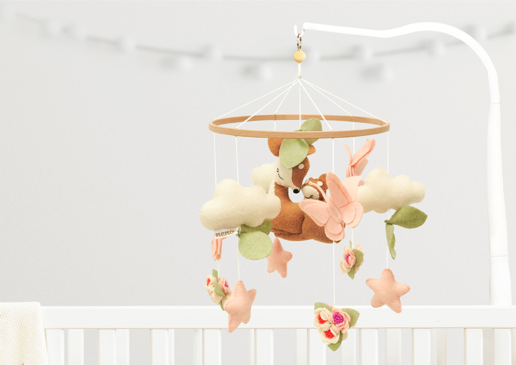 Karuzela Neno Rosi nad łóżeczkiem: sarenki, motylki i chmurki z filcu na drewnianym pierścieniu; ikony: łatwy montaż, ręcznie robione, rozwój wzrokowy, motoryka, uspokaja.